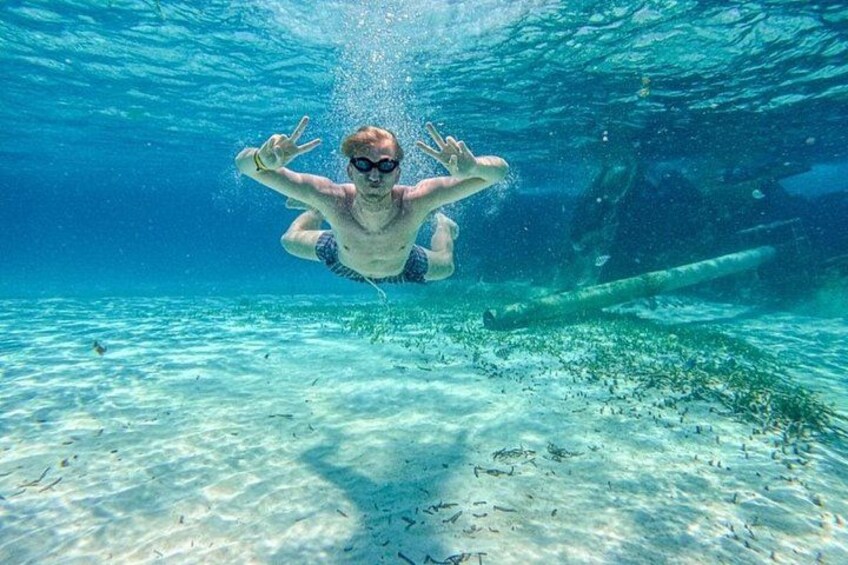 Una persona nada bajo el agua con una vista clara del fondo marino arenoso y unos restos hundidos. 2