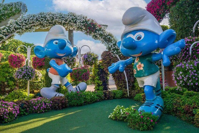 A large blue character statue in a garden with flowers and greenery. 2