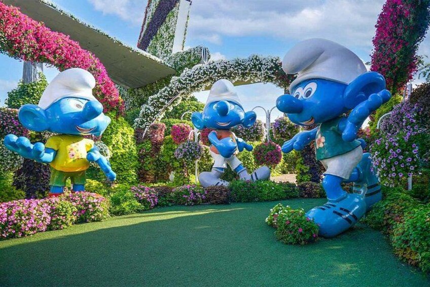 Large blue cartoon characters in a garden with flowers and a green pathway. 4