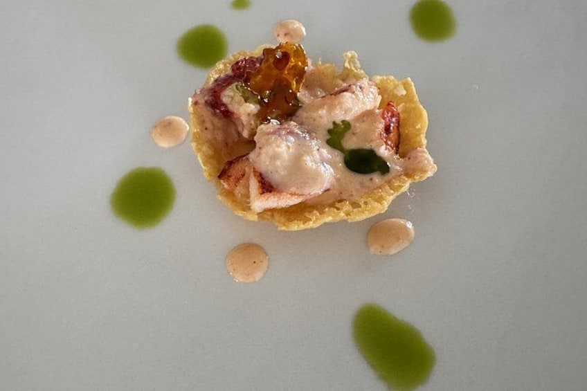 A dessert with a creamy topping, garnished with green herbs, on a white plate with green sauce dots. 1