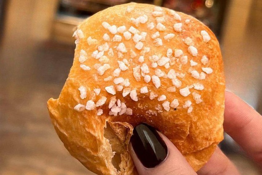 A hand holding a breaded food item with a golden-brown crust and white seasoning on top. 1