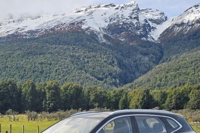 A car in a rural area with snow-capped mountains in the background. 4