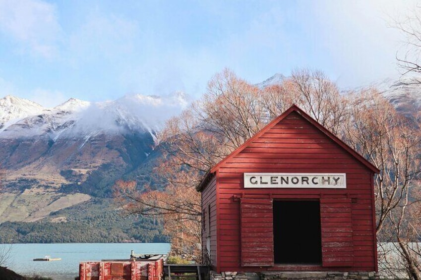 A red wooden building labeled 'Glenorchy' with a mountainous backdrop and a lake. 1