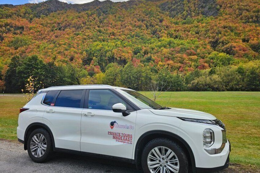 A white SUV parked on a road with a forested hillside in the background. 3
