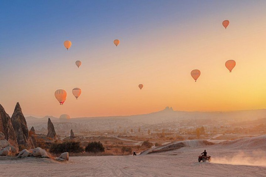 A desert landscape with hot air balloons, a rider on a dune buggy, and a mountain in the distance. 2