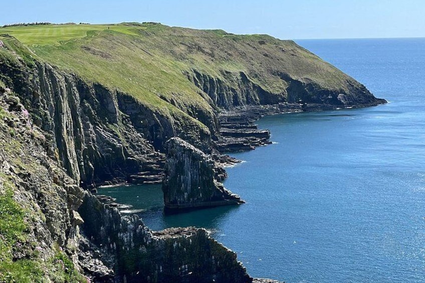 A coastal landscape with cliffs, a rocky outcrop, and calm sea. 1