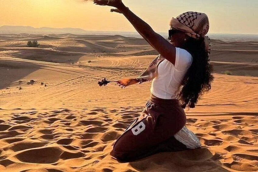 A person kneeling on sand dunes with a desert landscape in the background. 1