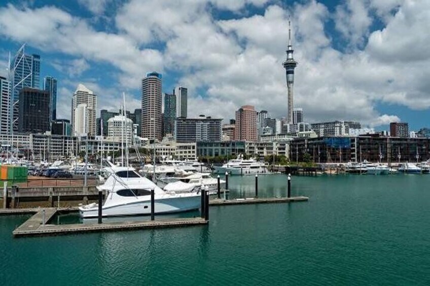 A marina with yachts docked, a city skyline with modern buildings, and a prominent tower in the background. 4