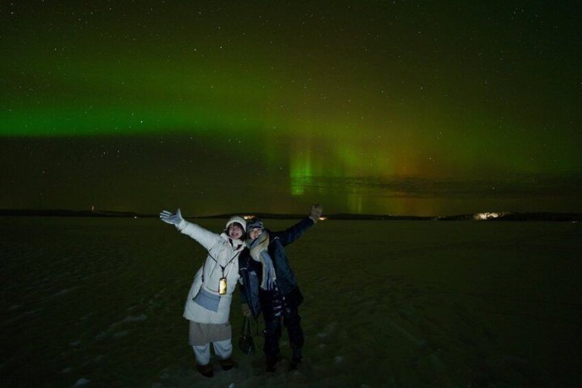 Two people standing on a snowy field with a green aurora in the background. 4