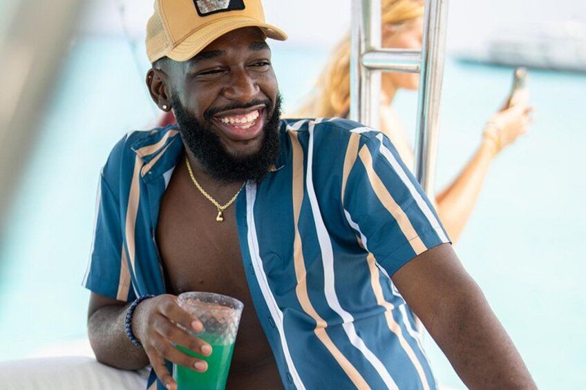 A person wearing a striped shirt and a cap, holding a green drink. 3