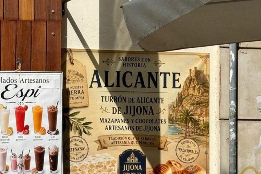 Un cartello con una pubblicità storica di Alicante, raffigurante un paesaggio costiero e artigianato tradizionale. 2