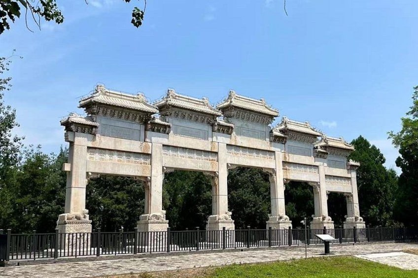 A large stone archway with intricate carvings and multiple columns, surrounded by a fence and greenery. 3