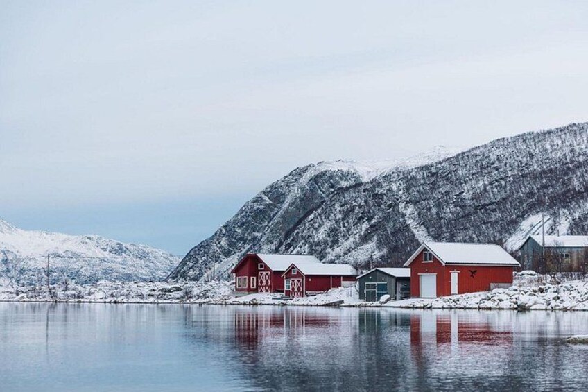 A snowy landscape with red buildings by a calm lake, surrounded by snow-covered mountains. 3