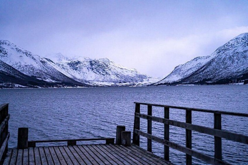 A wooden dock extending into a calm lake surrounded by snow-covered mountains. 5