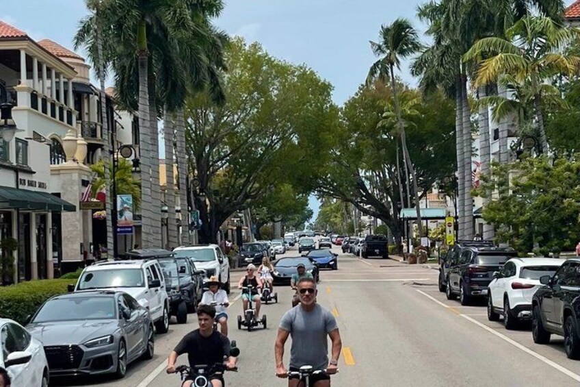 A street with parked cars, cyclists, and palm trees. 3