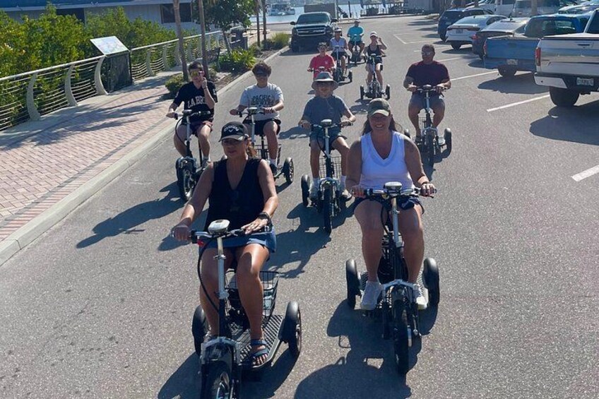 A group of people riding electric scooters on a paved road with cars parked on the side. 2