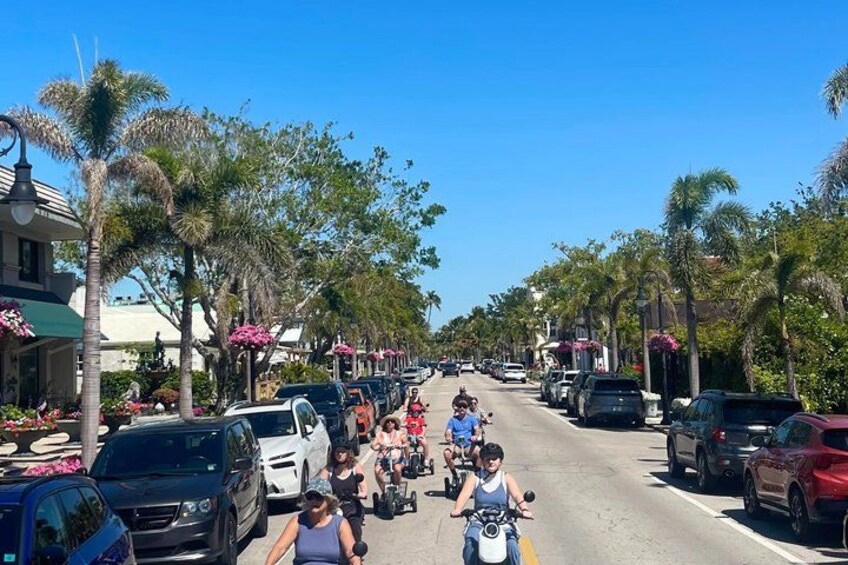 A street lined with parked cars and palm trees, with people riding motorcycles. 5