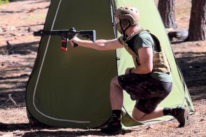 A person crouching next to a green tent in a wooded area. 3