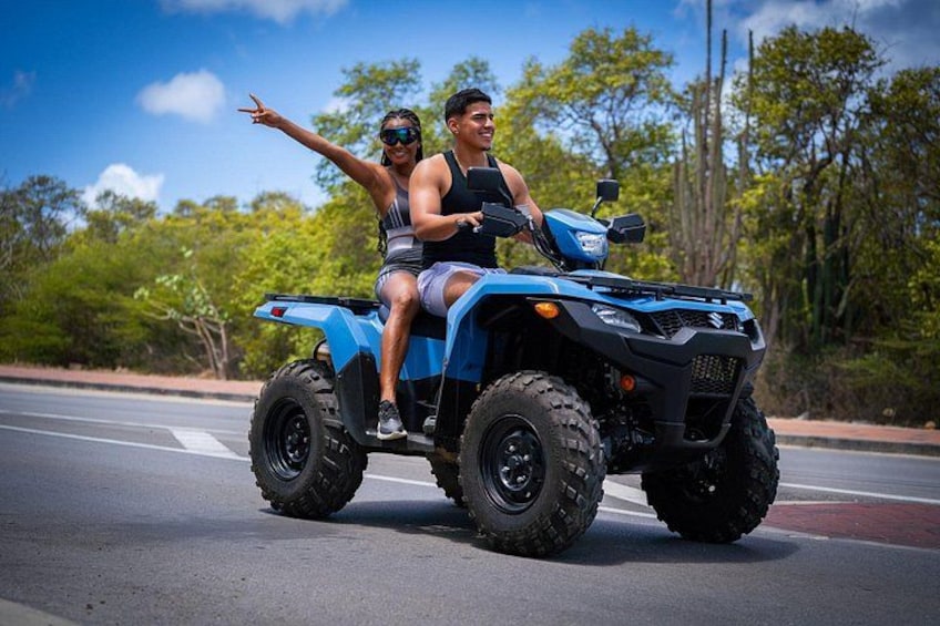 Two people on a blue ATV on a road with trees in the background. 2