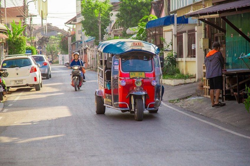 Un vehículo rojo de tres ruedas con la leyenda 'TAXI' en una calle con automóviles y un motociclista. 4