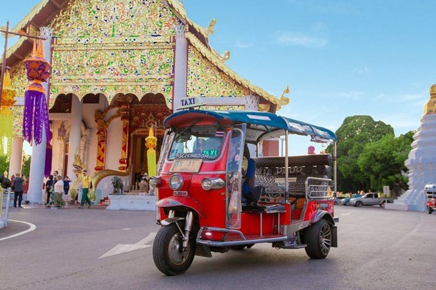 Un tuk-tuk rojo con toldo azul estacionado frente a un templo con decoraciones elaboradas. 1