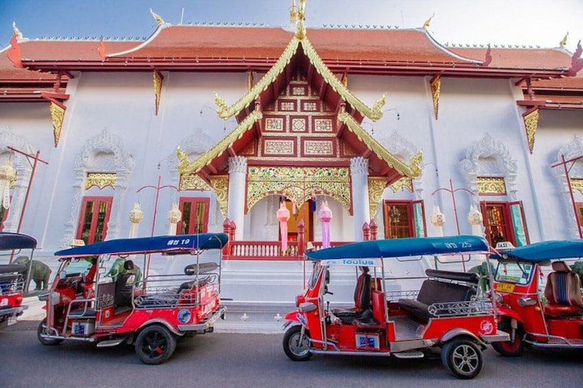 Un templo tradicional con arquitectura ornamentada, tuk-tuks estacionados al frente y un cielo despejado. 3