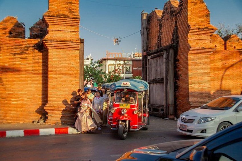 Un tuk-tuk, un coche blanco y un muro de ladrillo. 2
