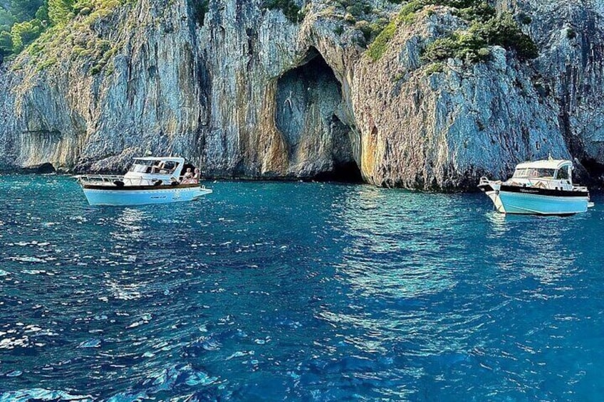 Two boats anchored near a rocky coastline with a cave formation. 2