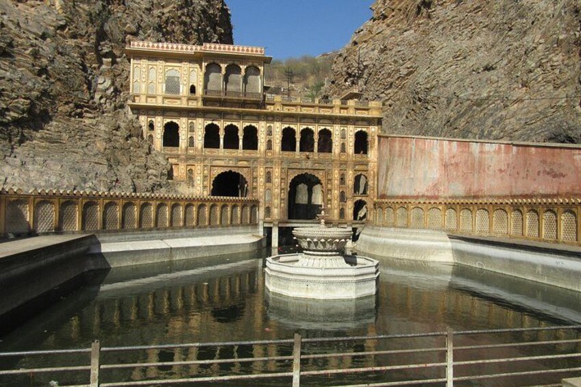 A historic building with intricate architecture, a large water body in front, and a rocky backdrop. 2