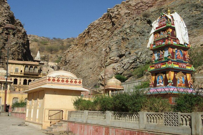 A temple with colorful decorations, a stone structure, and a rocky hillside in the background. 3