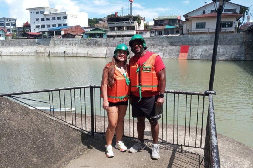 Two people wearing safety vests and helmets standing on a concrete platform by a body of water. 3