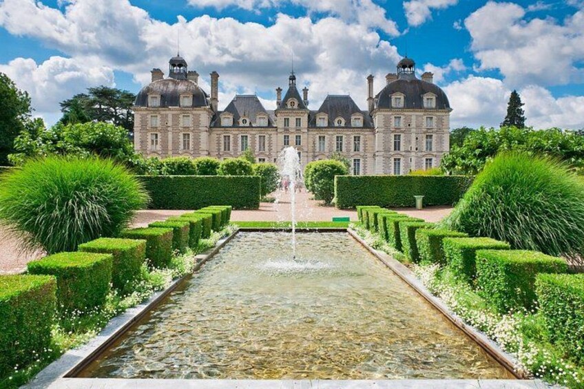A grand château with a symmetrical garden, a fountain, and manicured hedges. 5