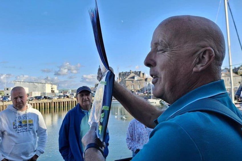 A man holding a large, colorful object, possibly a kite, with a waterfront and buildings in the background. 5