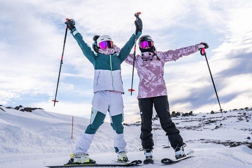Two people skiing on a snowy slope with their arms raised. 2
