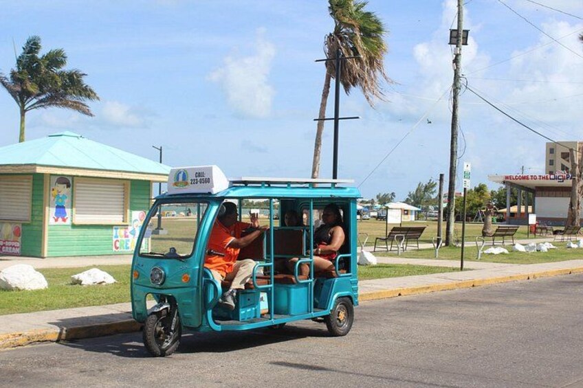A turquoise tuk-tuk on a street with palm trees and a small building in the background. 2