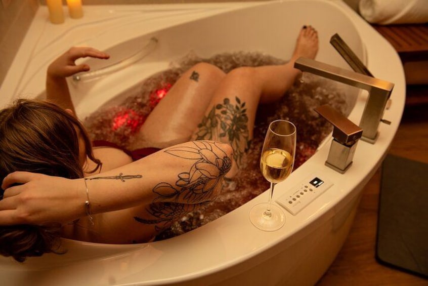 A person relaxing in a bathtub with a glass of wine and a remote control. 1