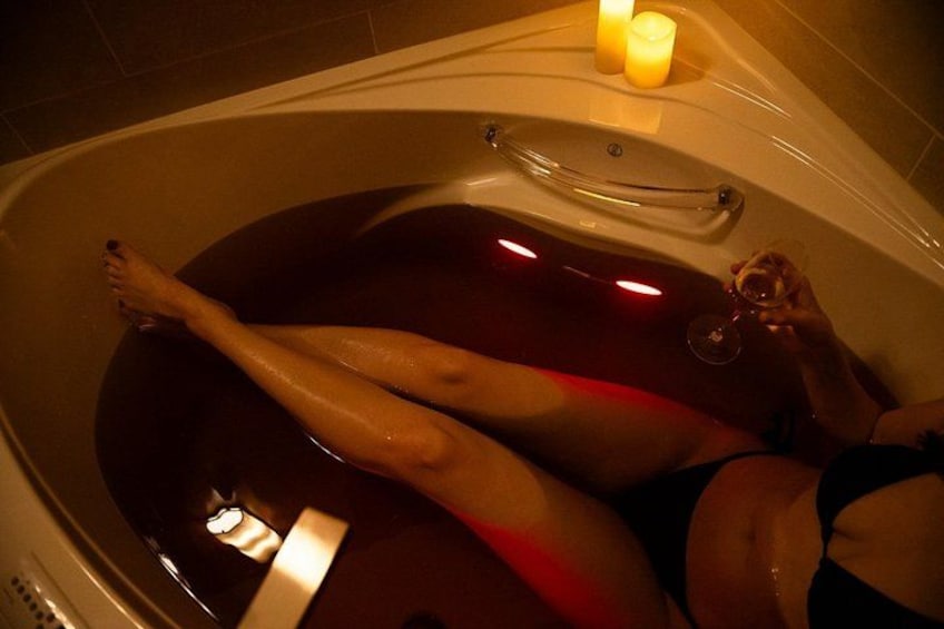 A bathtub with a person lying inside, a candle, and a glass of wine. 3