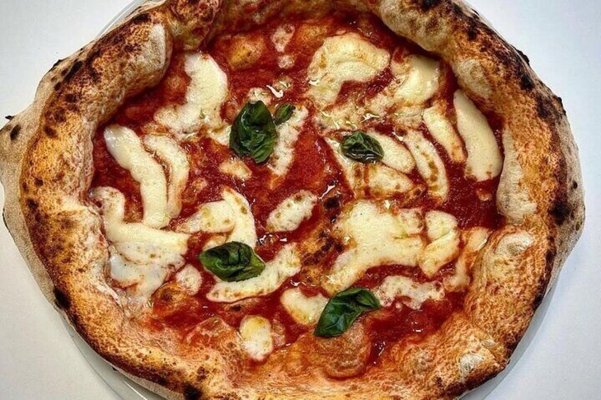 Une pizza recouverte de fromage fondu et de feuilles de basilic, servie sur une assiette blanche. 3