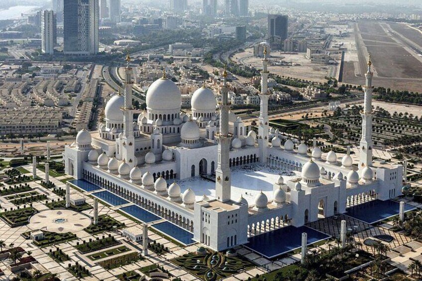 A large white mosque with multiple domes and minarets, surrounded by a well-maintained garden and urban landscape. 1