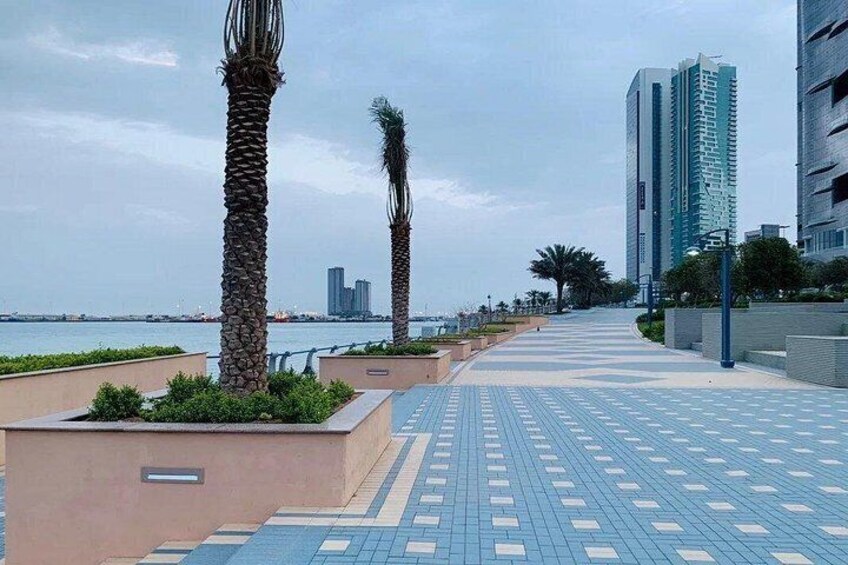 A waterfront promenade with palm trees, a tiled walkway, and high-rise buildings in the background. 3