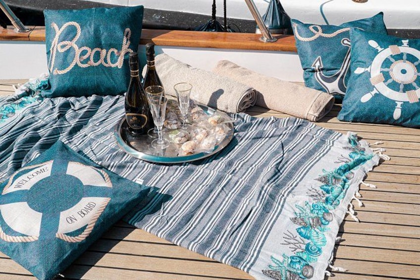 Een dek van een boot met een gestreepte deken, een fles champagne, glaasjes en een handdoek. 3