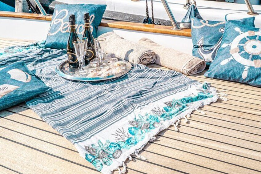 Un pont de bateau agrémenté d’un tapis à rayures bleues et blanches, d’un plateau avec des bouteilles et des verres, et de coussins assortis. 2
