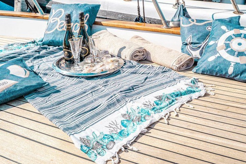Cubierta de barco con alfombra azul y blanca a rayas, una bandeja con botellas y vasos, y almohadas con motivos náuticos. 2