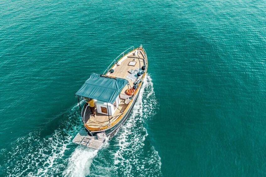 A boat with a covered deck, moving through turquoise water. 1