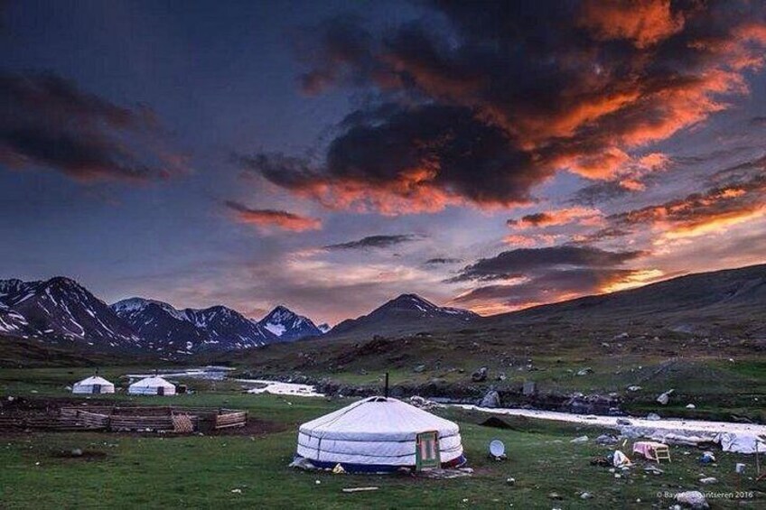 A yurt in a grassy field with mountains in the background. 1
