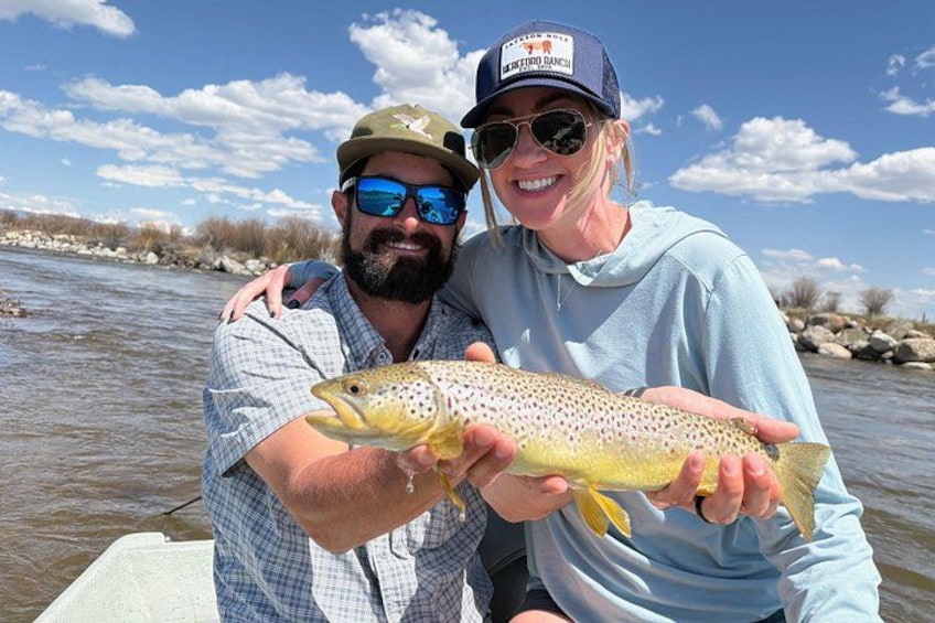 Two people holding a fish by a river. 2