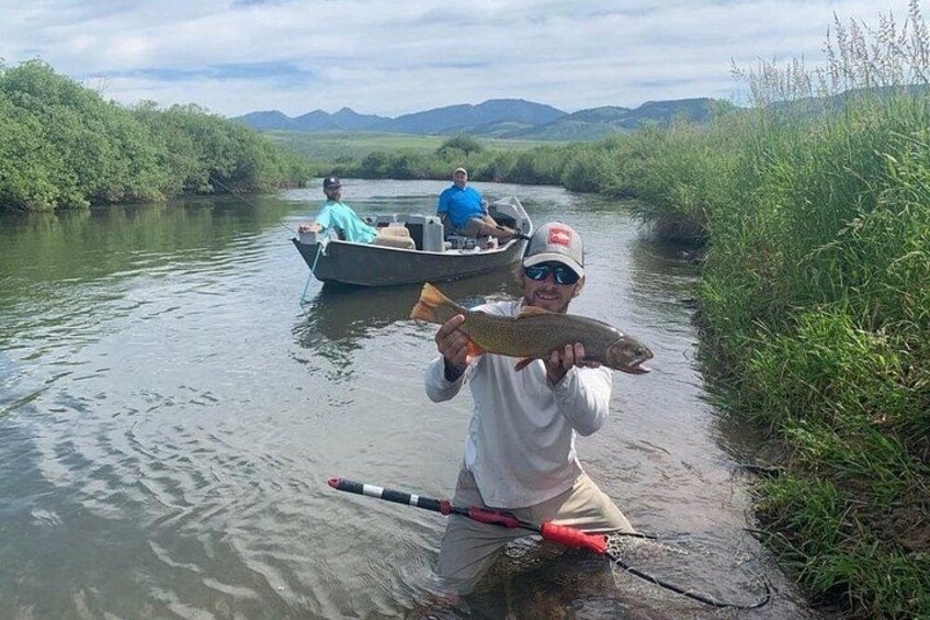 Une personne tenant un poisson, se tenant près d’un bateau et d’une canne à pêche, sur une rivière. 4