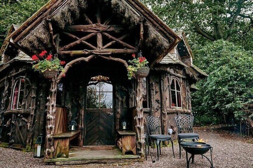 A rustic wooden house with a thatched roof, a wooden door, and a small outdoor seating area with a table and chairs. 2