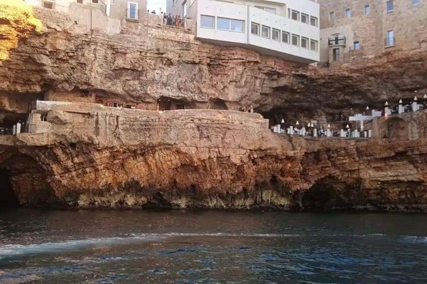 A rocky cliff with a building on top and a body of water in the foreground. 2