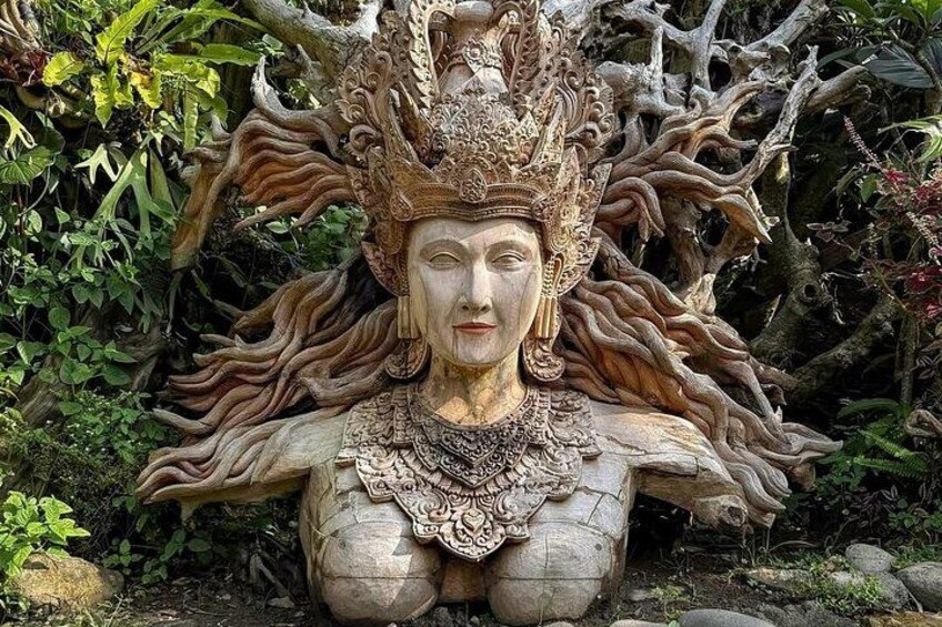 A detailed sculpture of a figure with elaborate headdress and jewelry, set against a backdrop of natural foliage and tree roots. 4
